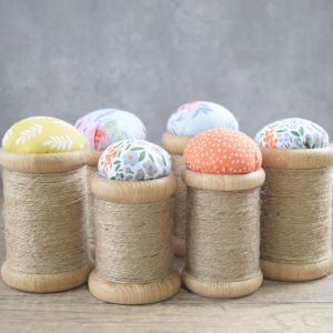 a selection of wood turned pin cushions shaped to look like cotton reels and finished with a colourful cotton cushion top and natural twine.