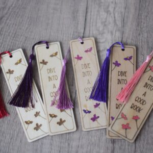 a photo showing five wooden laser engraved bookmarks. The bookmarks are hand painted in shades of pinks and purple