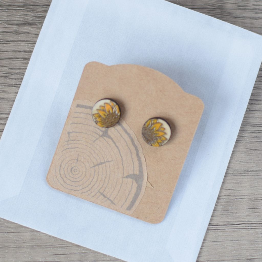 Top view of wooden stud earrings on a kraft card backing and glassine bag.
