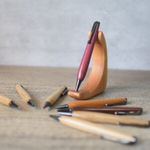 photo showing a selection of slim wood turned pens with one pen displayed on a wooden stand