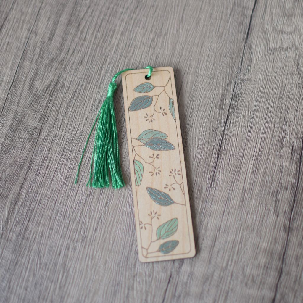 A single wooden laser engraved bookmark with a leaves design. Th bookmark has been hand painted with shades of metallic green with a green silky tassel