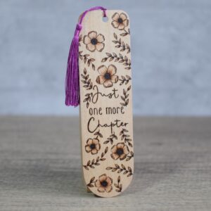 Photo showing a upright wooden bookmark with a purple silky tassel. The bookmark features a text and blossoms design. The text reads "one more chapter".